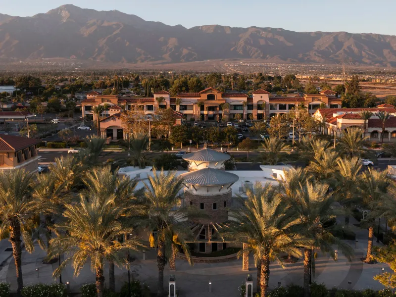 Palm trees surrounding a circular building with mountains in the background at sunset.