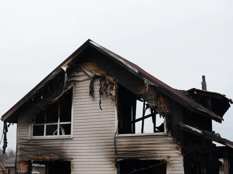 Partially burned two-story house with damaged siding and broken windows.