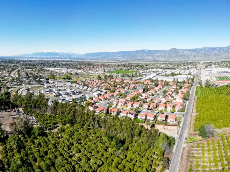 Aerial view of a suburban neighborhood beside orchards and mountains.