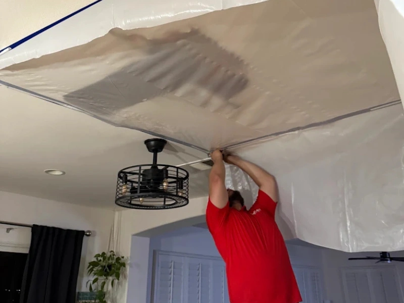 Person in red shirt installing plastic sheeting on a ceiling.