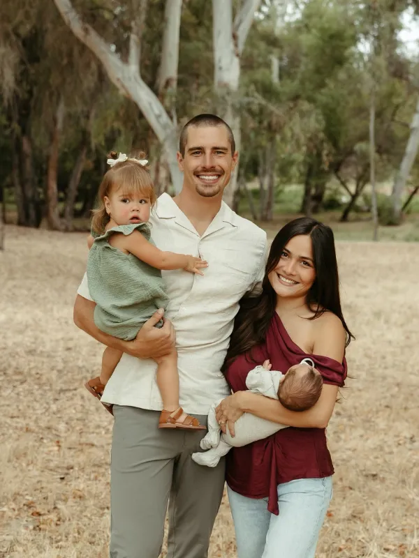 Family of four posing outdoors, parents holding two young children.