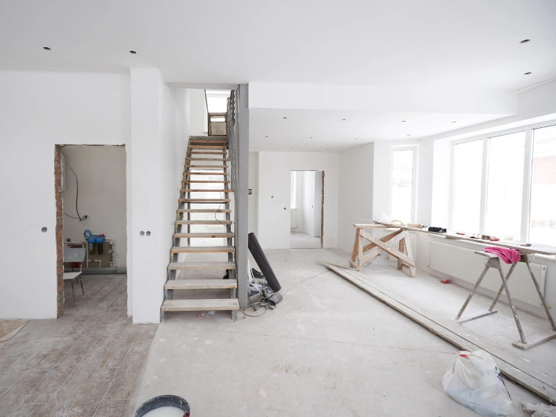 Unfinished interior room with wooden stairs, construction materials, and large windows.