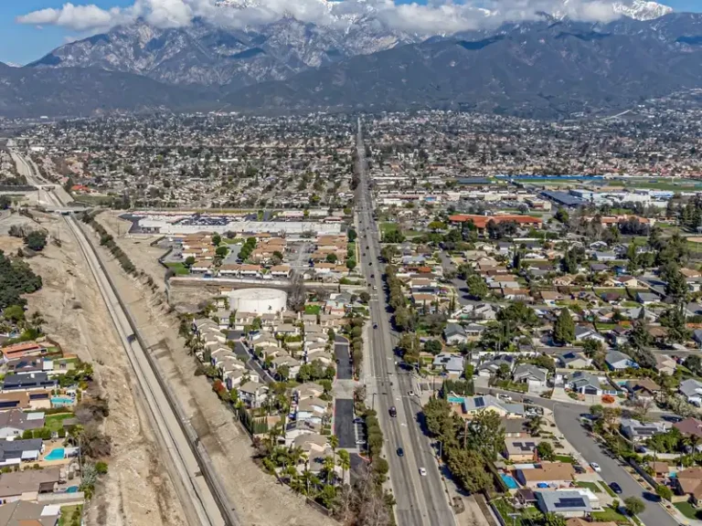 Aerial view of a suburban city with a long straight road and mountains in the background.