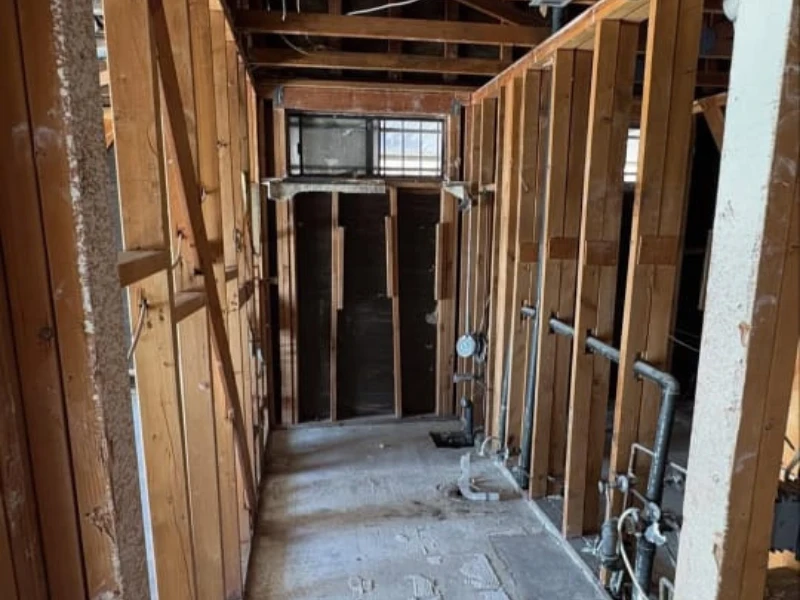 Exposed framing in a gutted hallway with plumbing pipes.