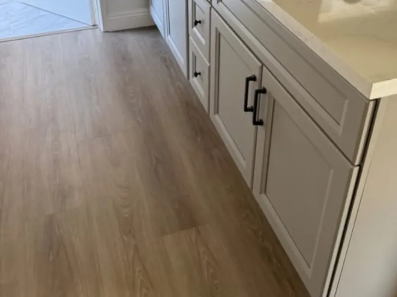 Wooden kitchen floor beside white cabinets with black handles.