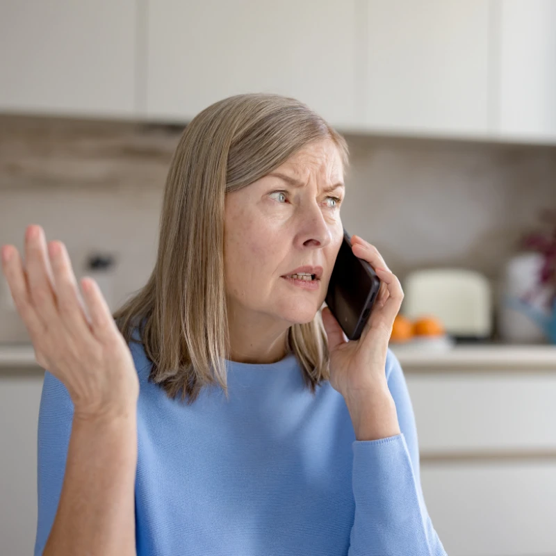 Frustrated woman talking on a smartphone in a kitchen.