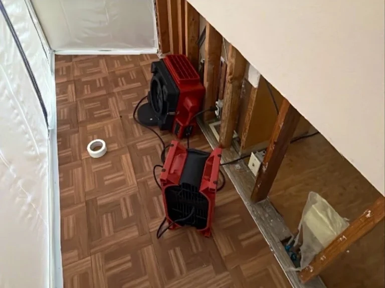 Two red fans drying a damaged wall and floor.